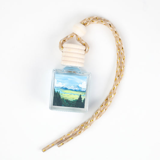 Nature-themed car air freshener, glass bottle, scenic mountain design, braided rope hanger.