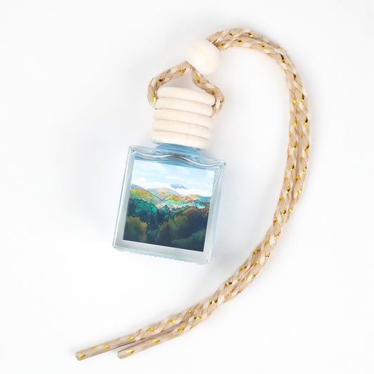 Blue glass air freshener bottle with scenic landscape design and braided beige rope tassel.
