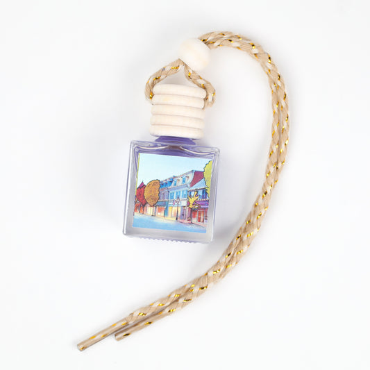 Purple glass car air freshener with braided rope and wooden cap, featuring a colorful street scene design.