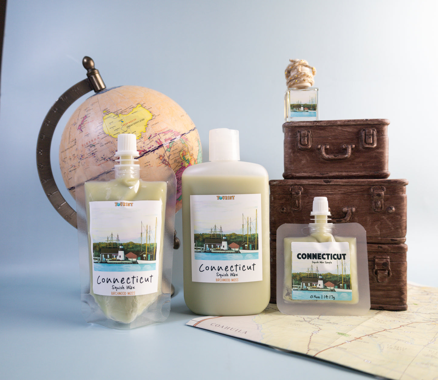 Three bottles labeled 'Connecticut' with a globe and suitcases in the background on a light blue surface.