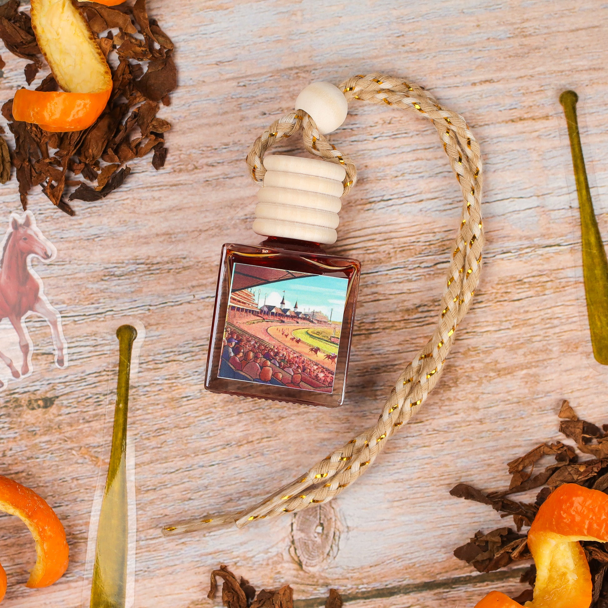 Decorative air freshener bottle, amber color, wood cap, featuring a horse racing scene, with braided rope hanger.