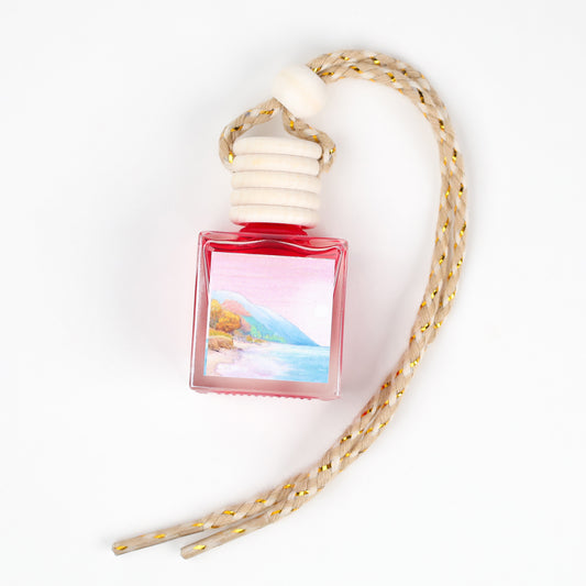 Red glass car air freshener with nature-themed label and braided rope hanger.