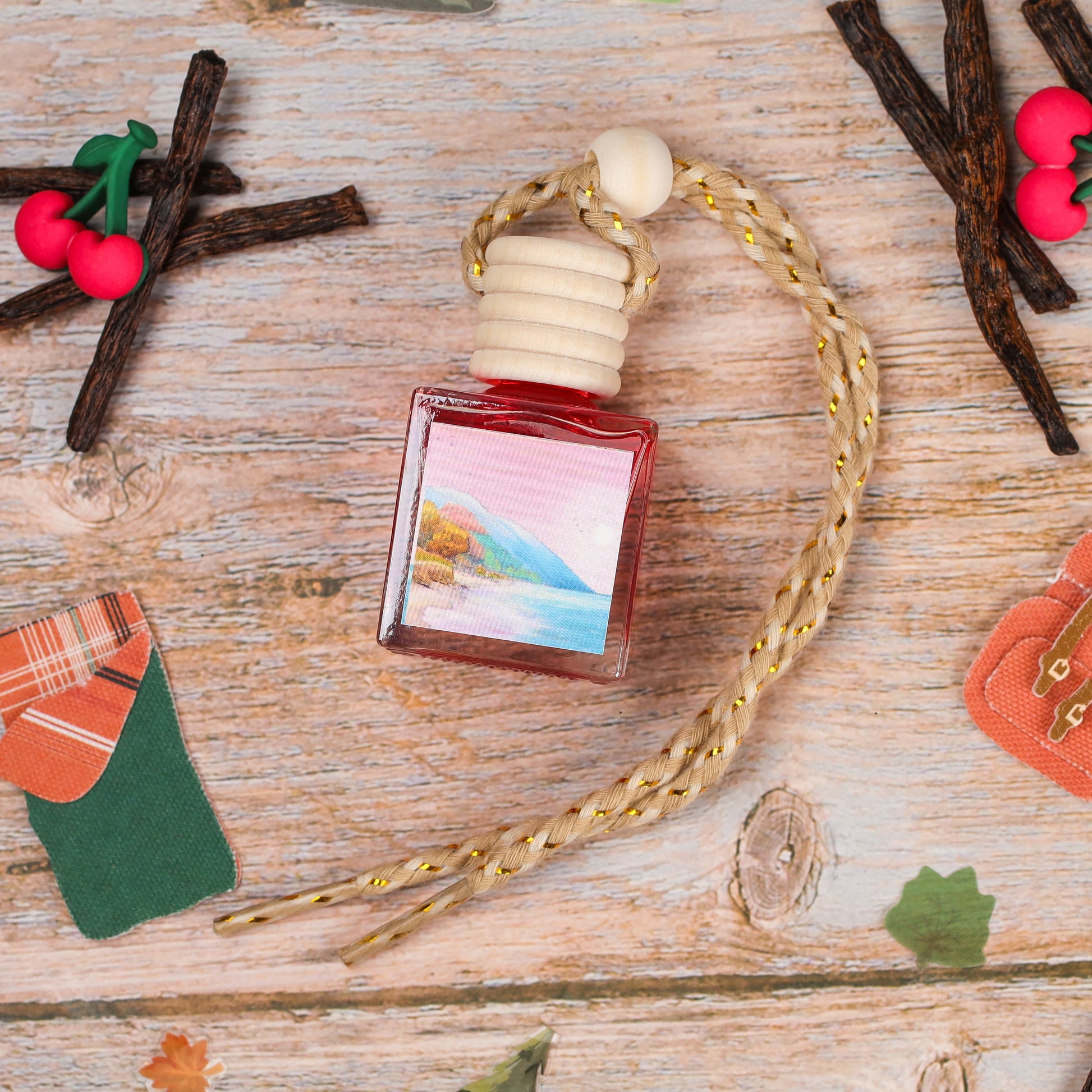 Small red glass air freshener bottle with beach landscape label and natural rope hanging