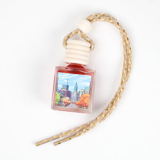 A red scented car air freshener with a city skyline design and a decorative braided hanger.
