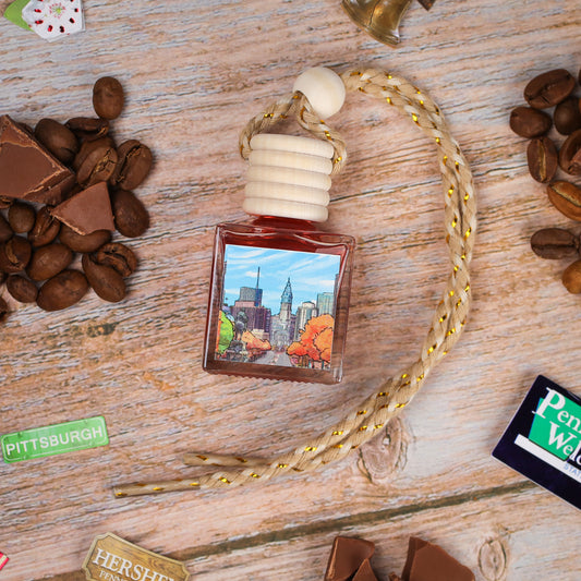 Artistic fragrance bottle with wooden cap, featuring cityscape label, surrounded by coffee beans and chocolate.