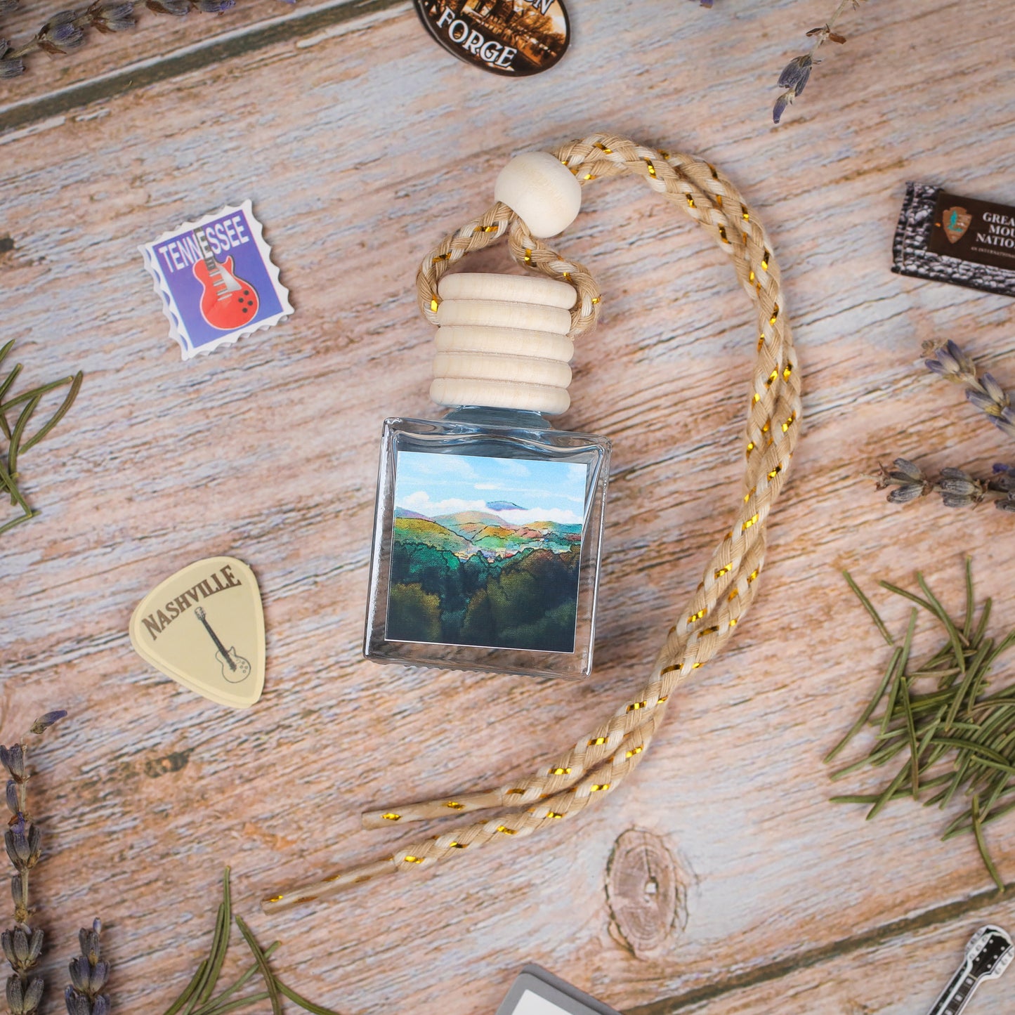 Scenic landscape car air freshener, blue glass bottle with braided rope, handcrafted with natural oils.