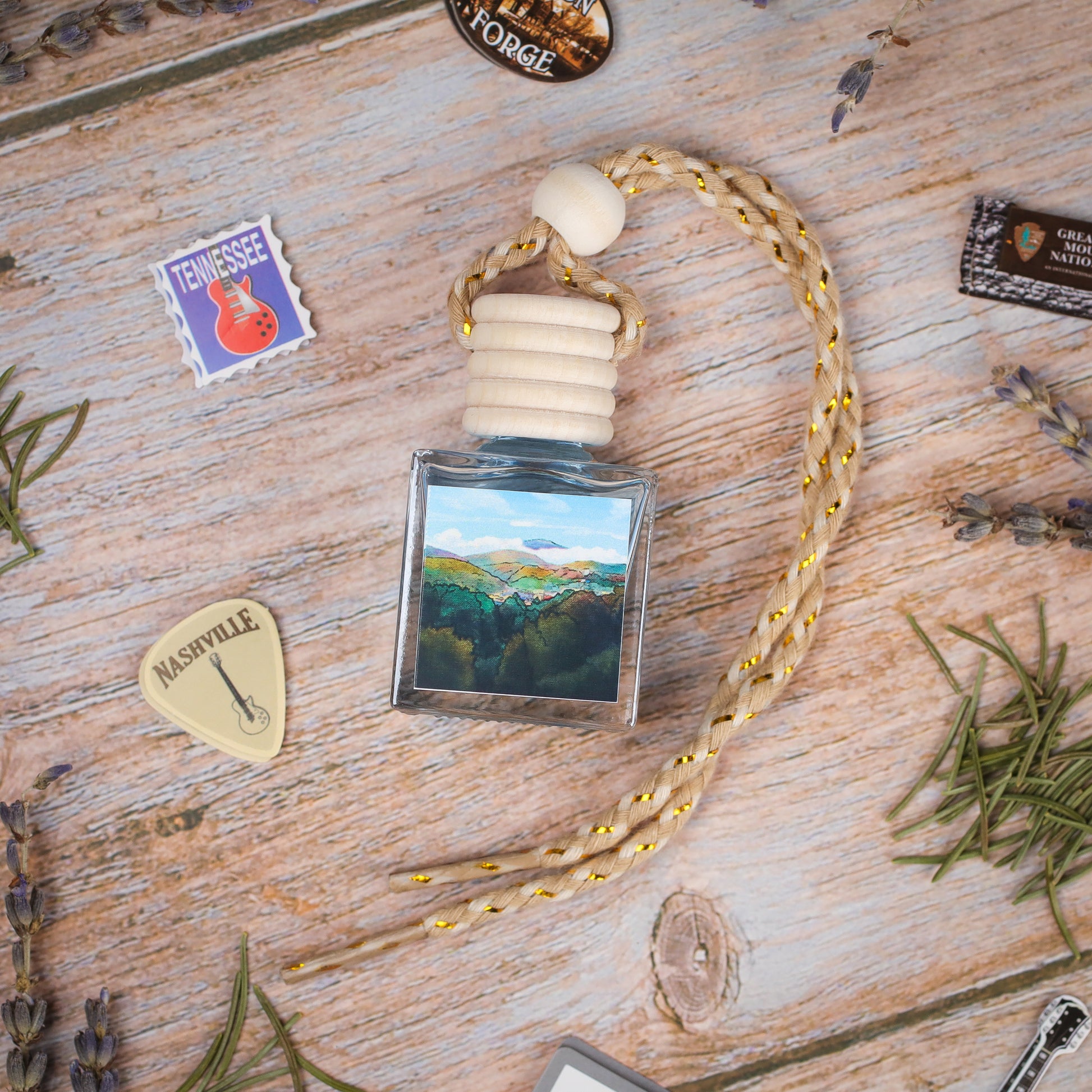 Scenic landscape car air freshener, blue glass bottle with braided rope, handcrafted with natural oils.