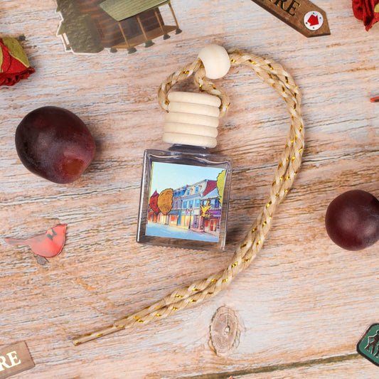 Artistic glass car air freshener with a braided rope, featuring a colorful town illustration.