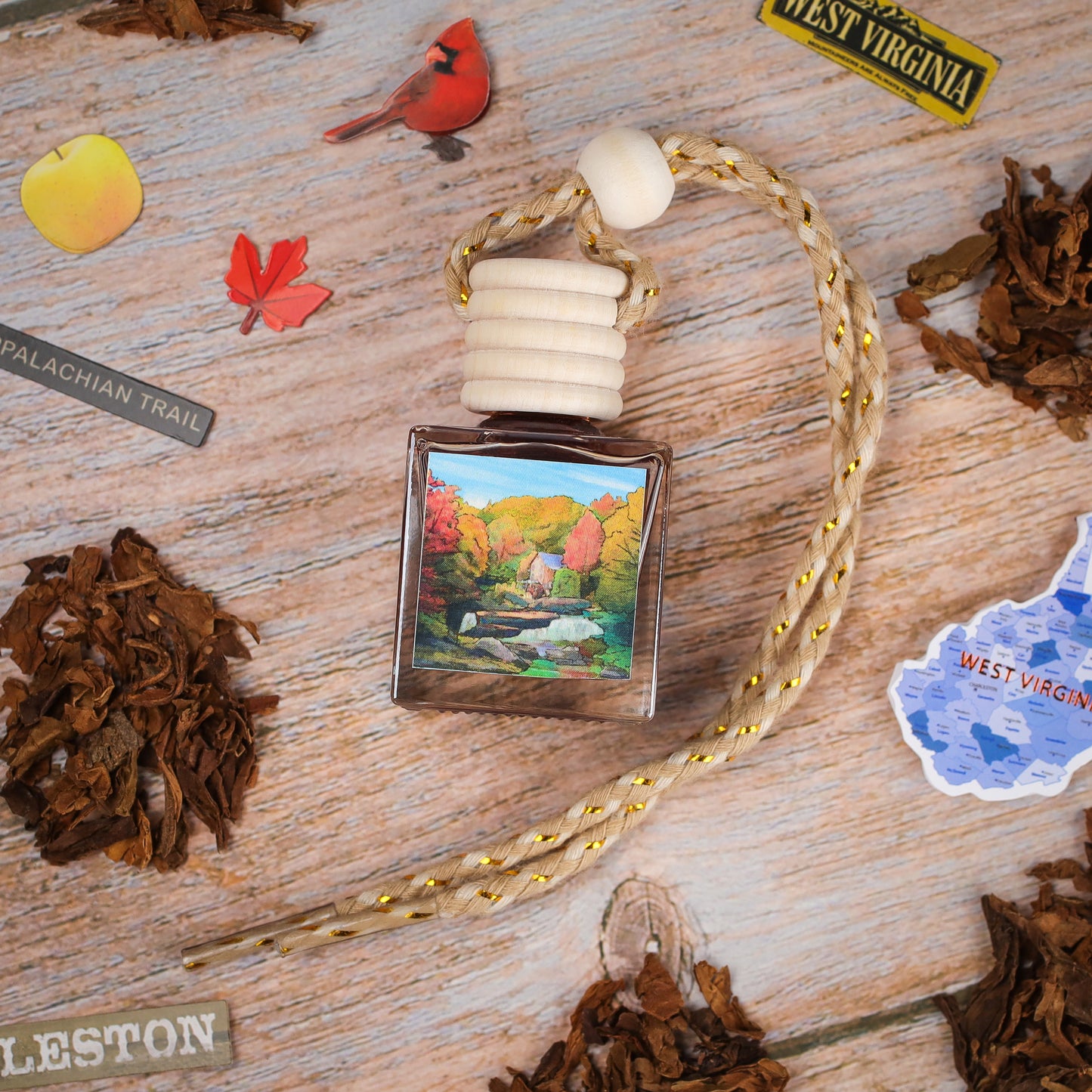 Handcrafted car air freshener, square glass bottle, nature artwork design, featuring fall colors and wooden cap.